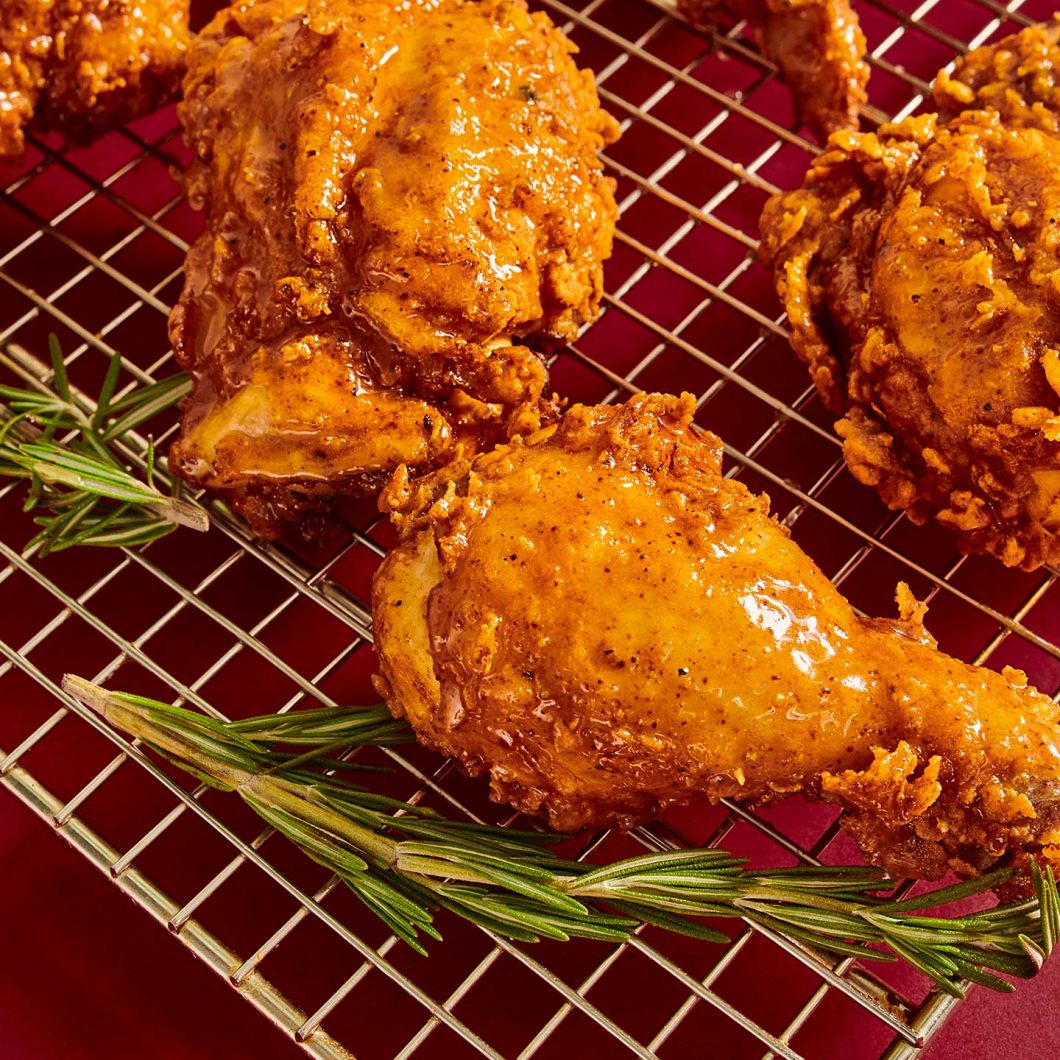 3 honey butter fried chicken pieces on a wire rack with rosemary next to the chicken