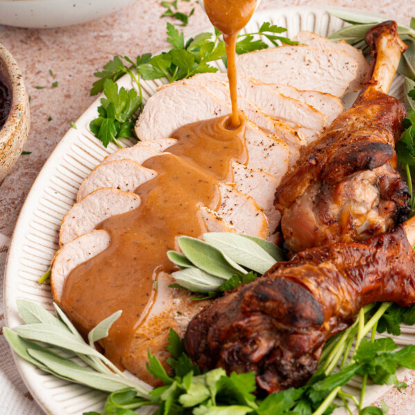 Turkey gravy from drippings is poured over sliced turkey breast for serving.