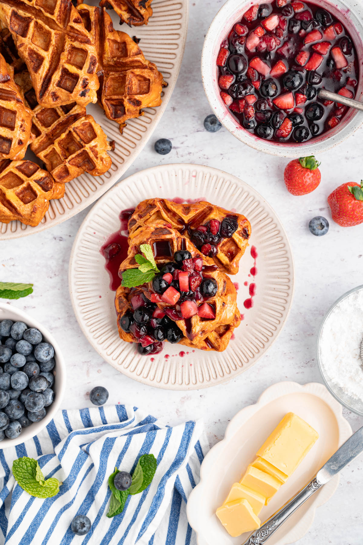 French toast waffles with berry compote on a white plate with the remaining french toast sitting on a plate to the side.
