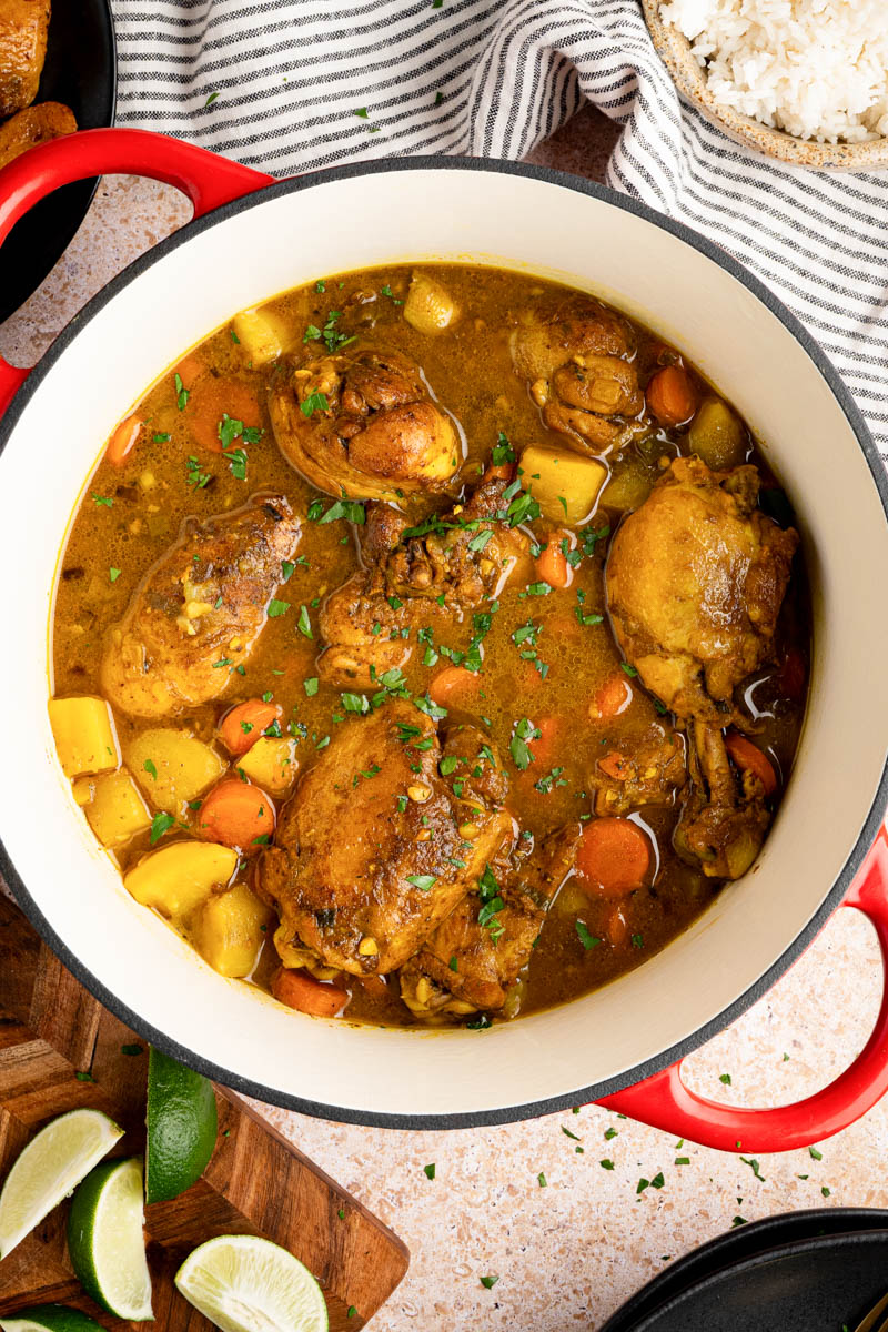 Chicken curry in a pan after cooking with a plate of fresh cooked rice and lime wedges off to the side. 