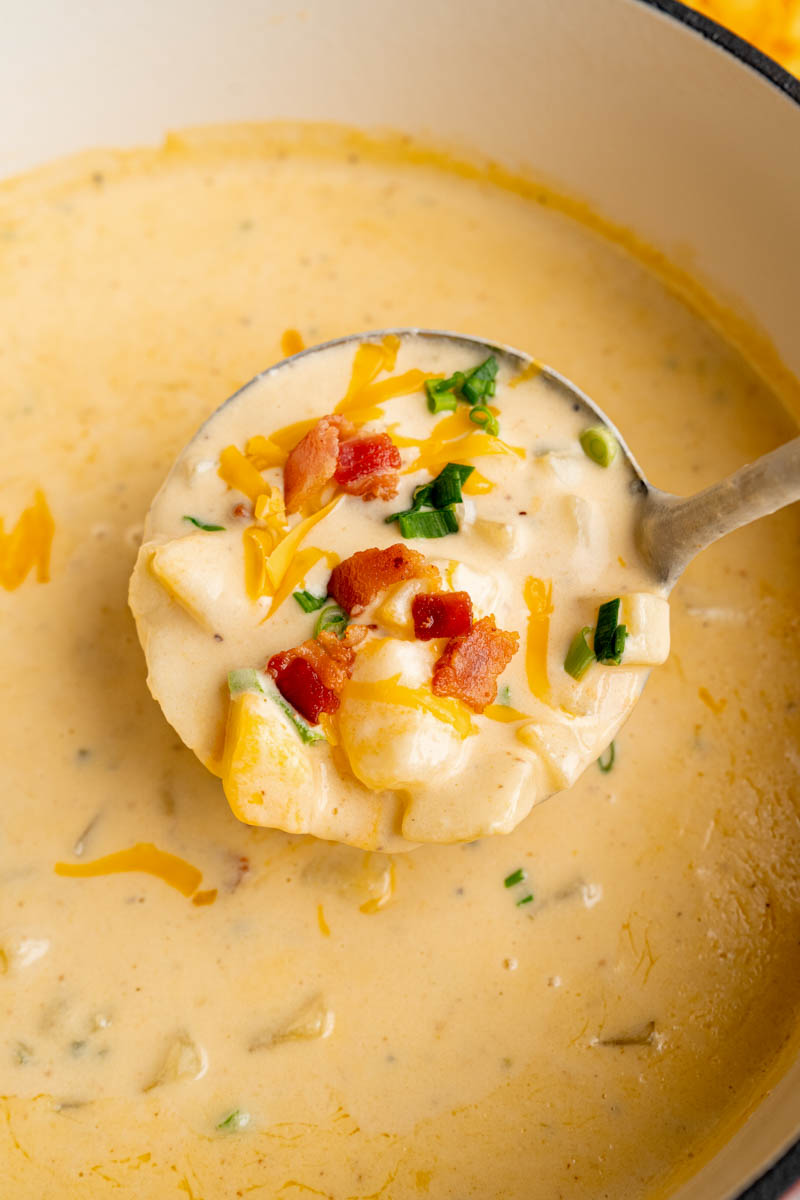 A ladle scoops loaded baked potato soup from the pan.