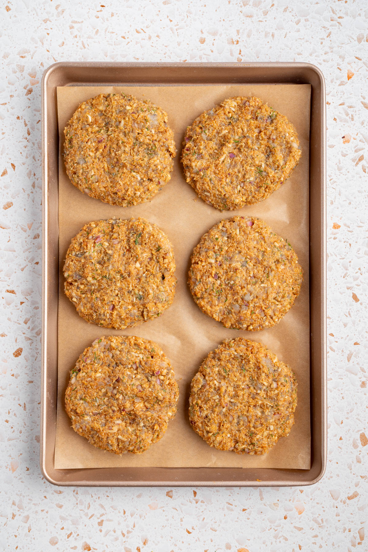 Six shrimp patties shaped on a baking sheet before cooking.