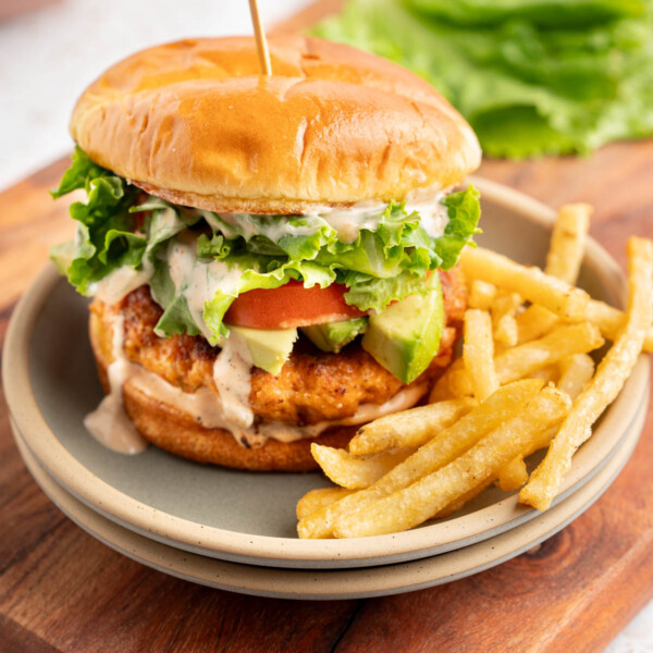 A shrimp burger on a plate with fries on a tabletop.