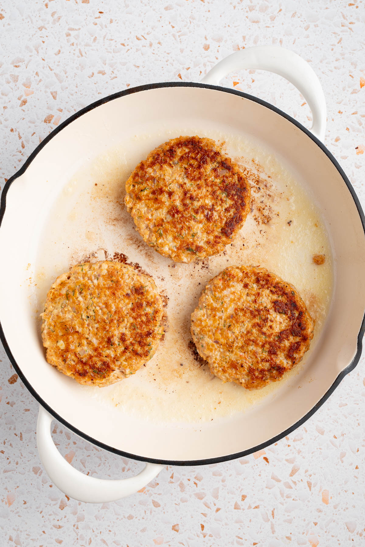 Three shrimp burgers in a skillet while searing.