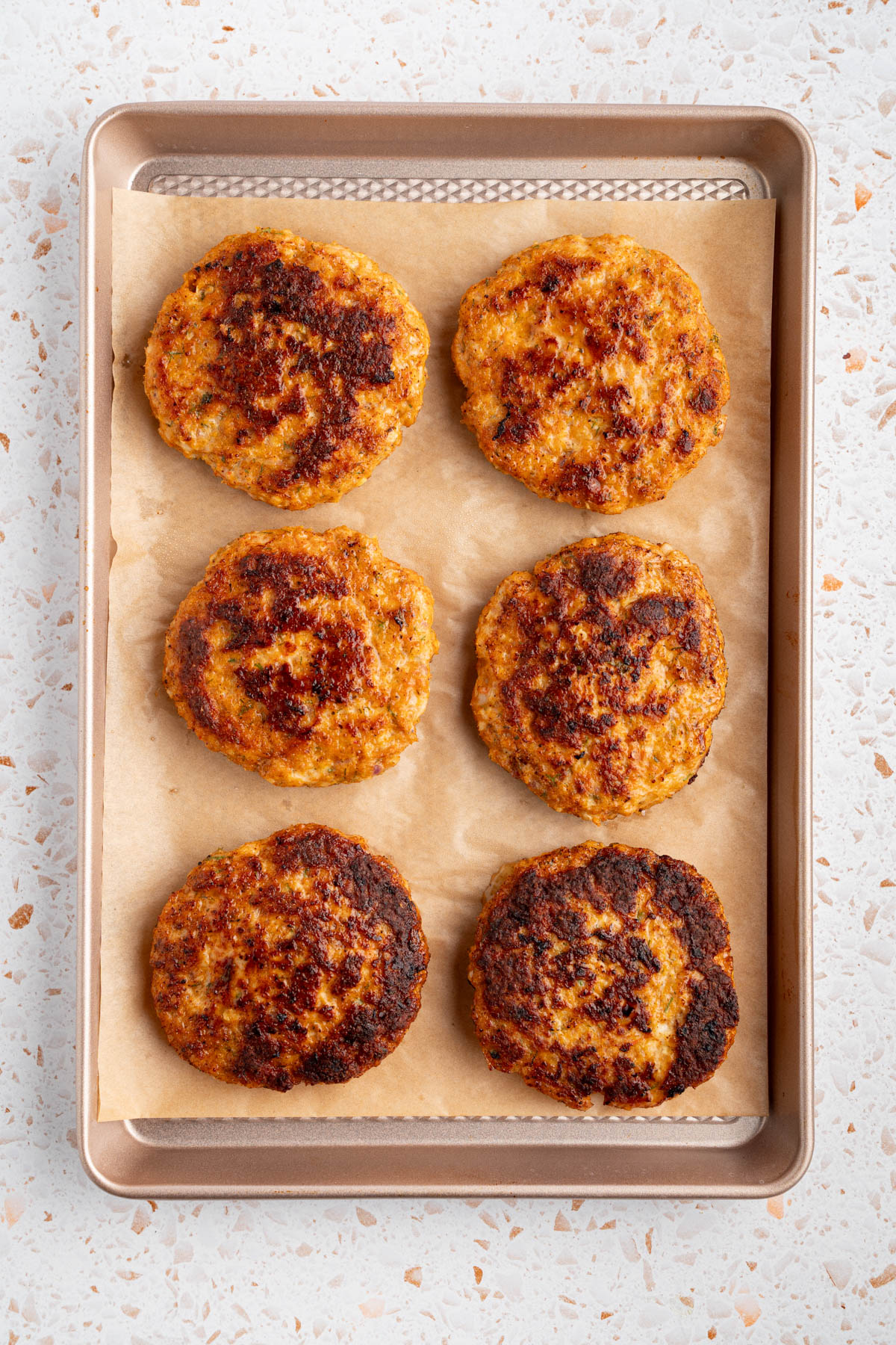 Six shrimp patties on a baking sheet before going into the oven to finish cooking.