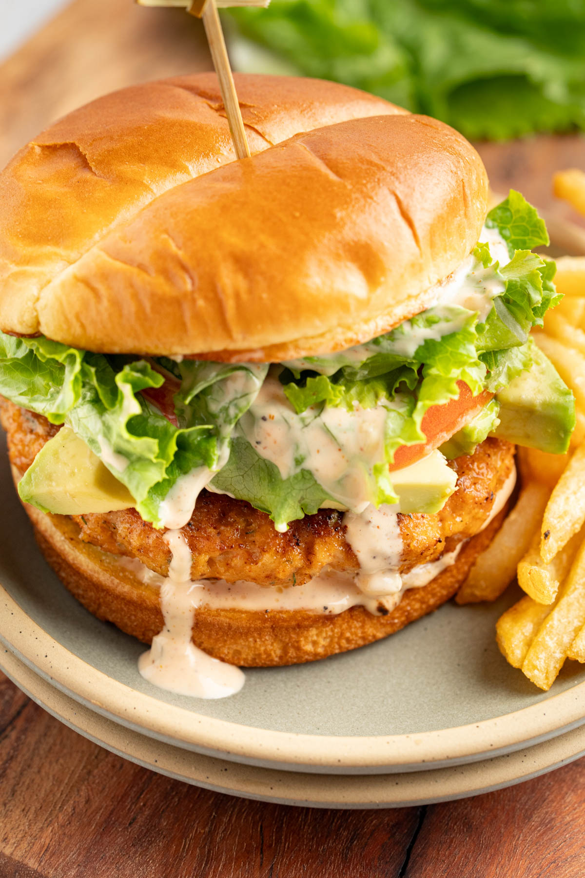 A shrimp burger on a bun with lettuce, tomato, and sauce.