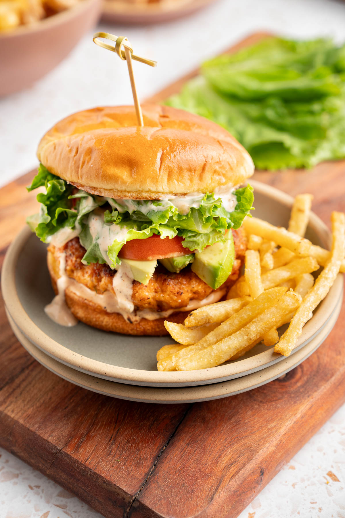 A shrimp burger on a plate with fries on a tabletop.