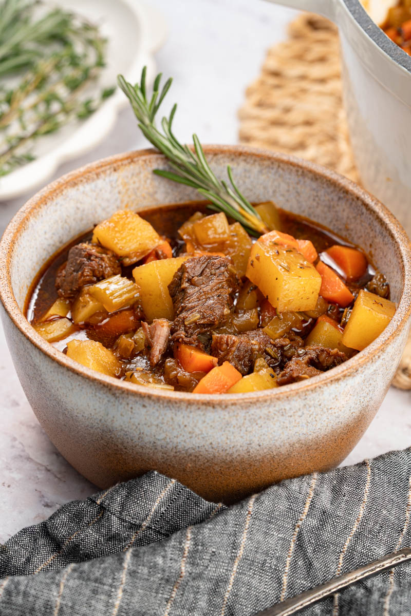 a bowl of hearty beef stew sits on a white countertop for serving.