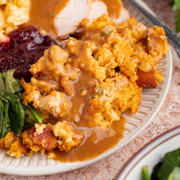 Cornbread dressing on a plate with turkey, cranberry sauce, greens and mashed potatoes.