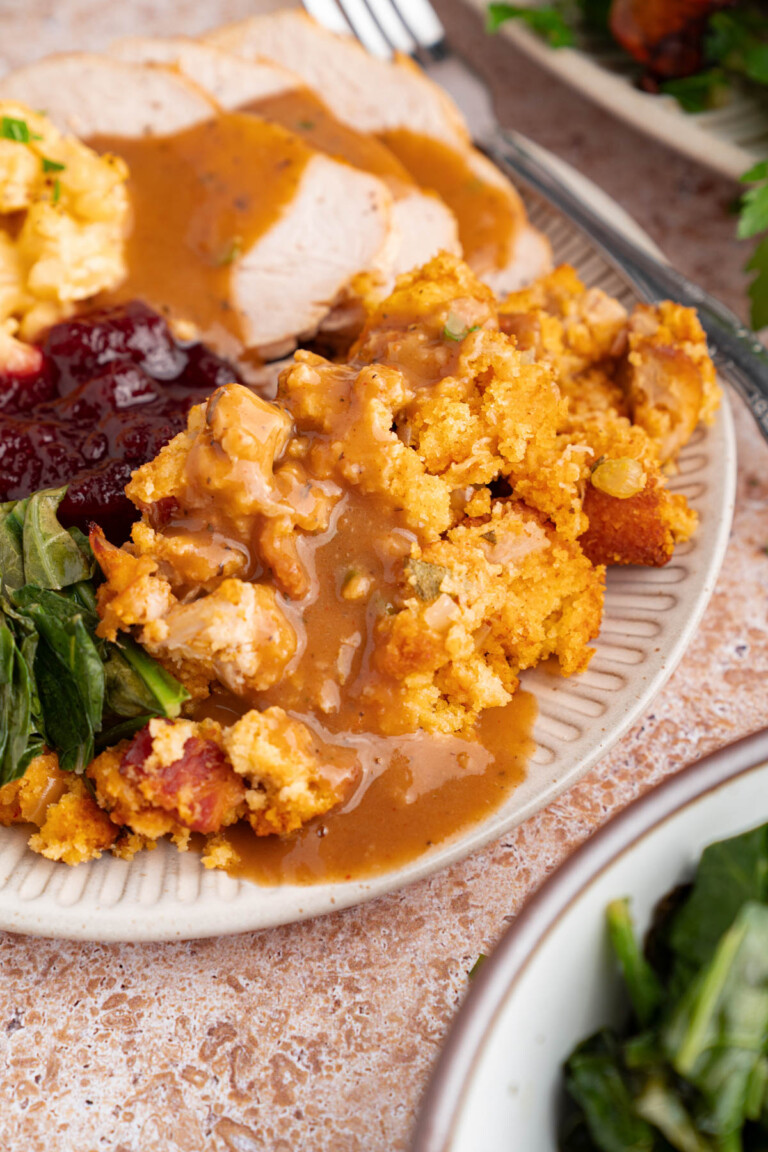 Cornbread dressing on a plate with turkey, cranberry sauce, greens and mashed potatoes.