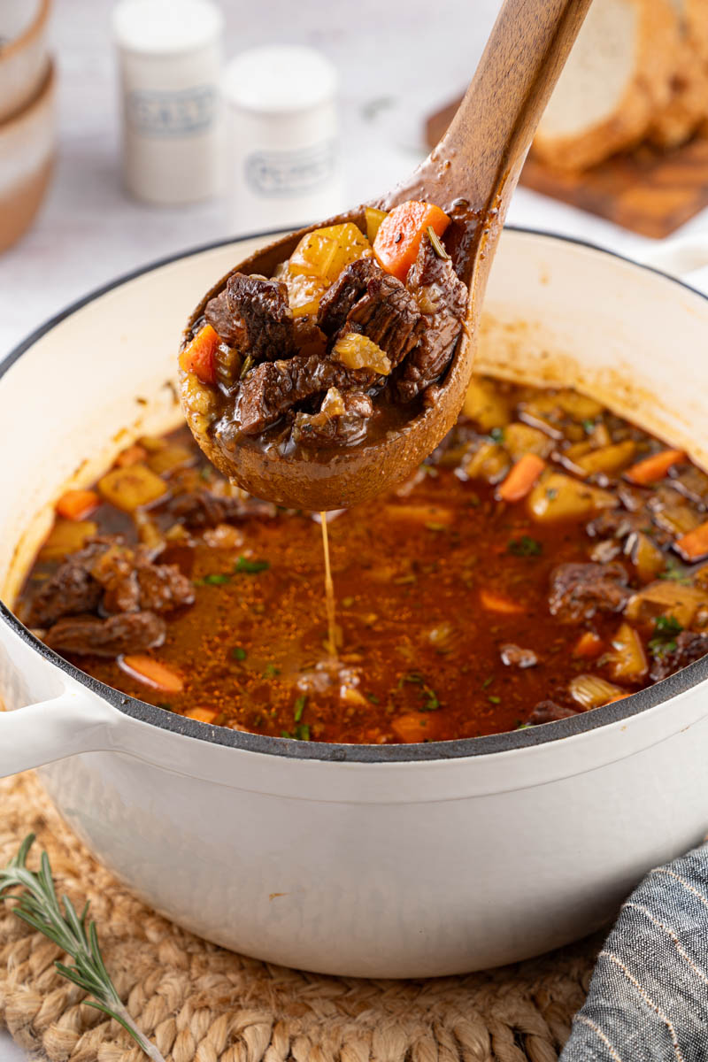 A large spoon lifts up a scoop of beef stew from the Dutch oven for serving.