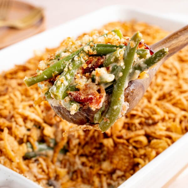 A spoon scoops fresh green bean casserole from a dish for serving