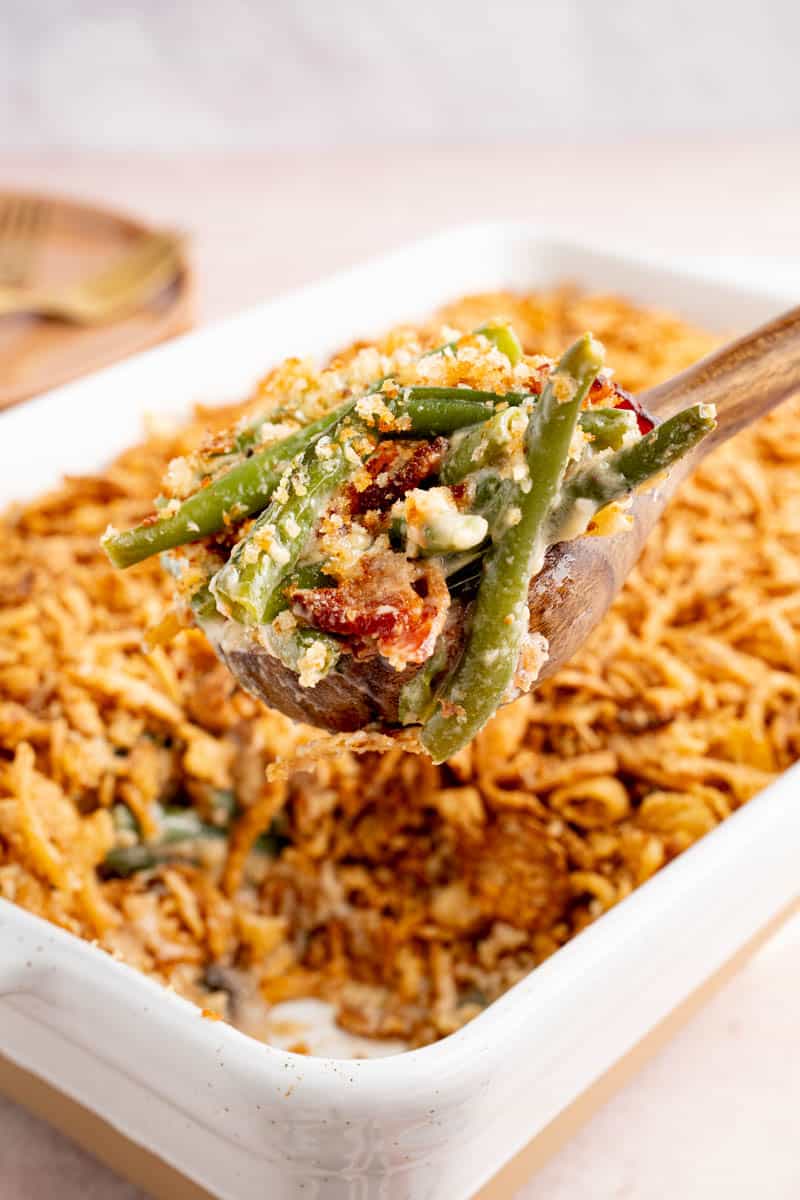 A spoon scoops fresh green bean casserole from a dish for serving