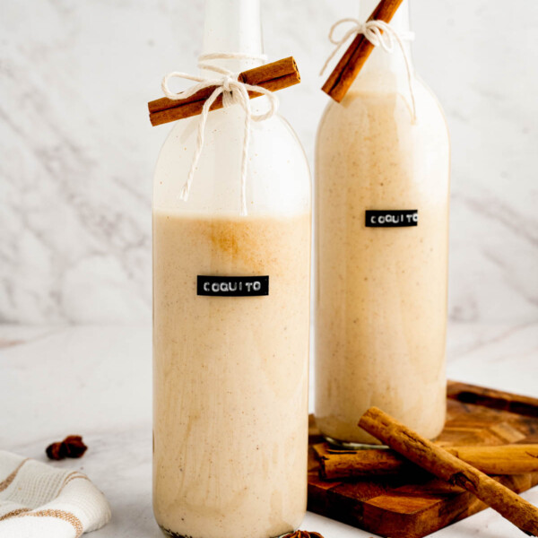 A bottle of coquito labeled and with a piece of cinnamon tied around it.