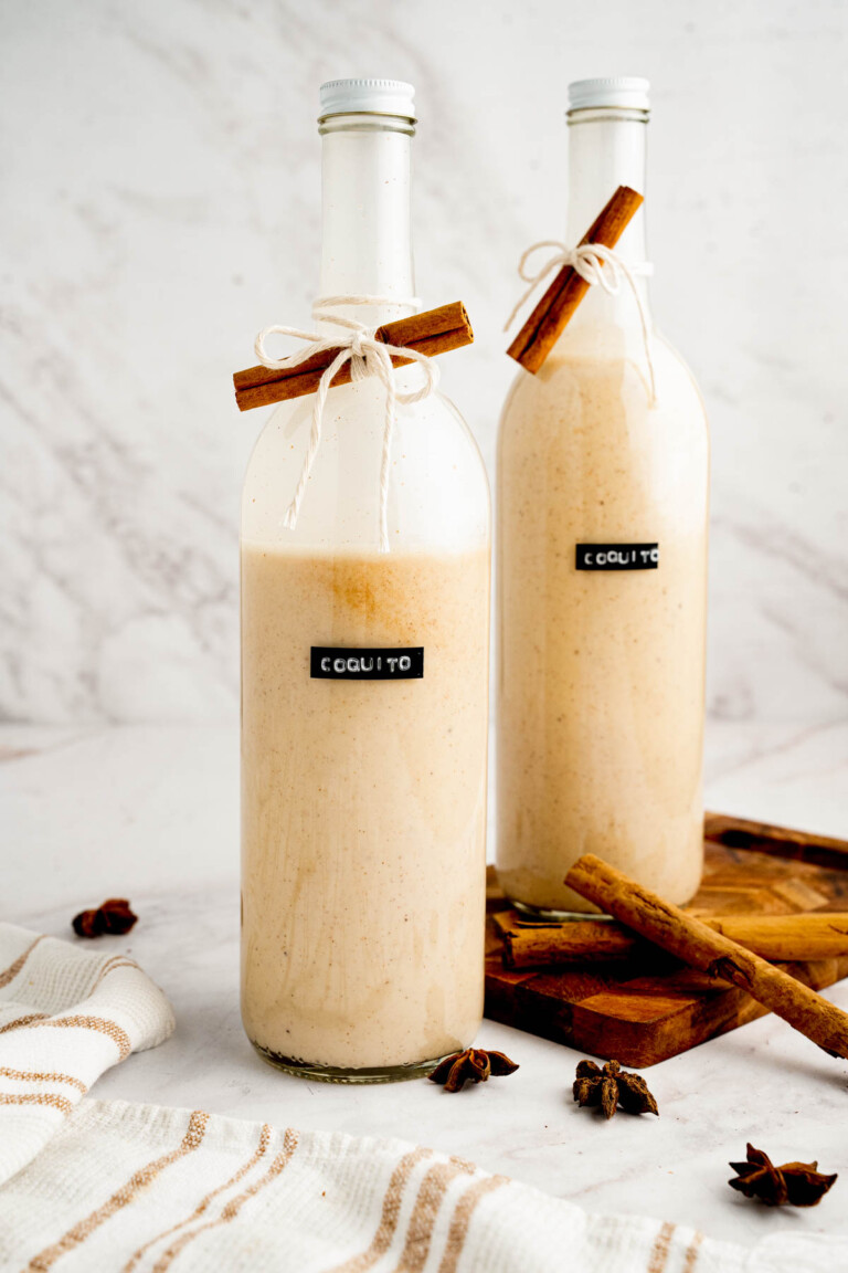 A bottle of coquito labeled and with a piece of cinnamon tied around it.