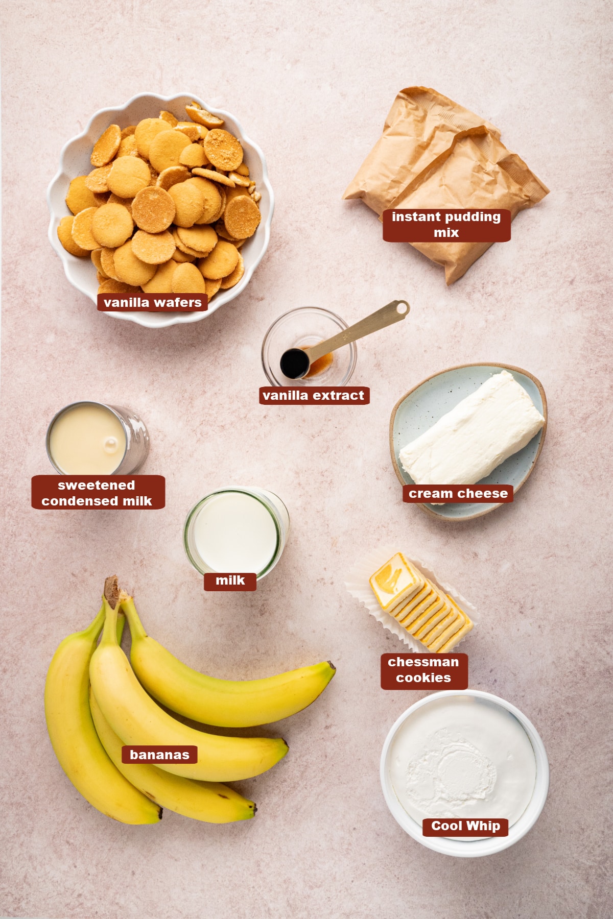 All of the ingredients for banana pudding in bowls on a countertop including vanilla wafers, vanilla instant pudding mix, sweetened condensed milk, cream cheese, milk, vanilla extract, Cool Whip, bananas and chessman cookies.