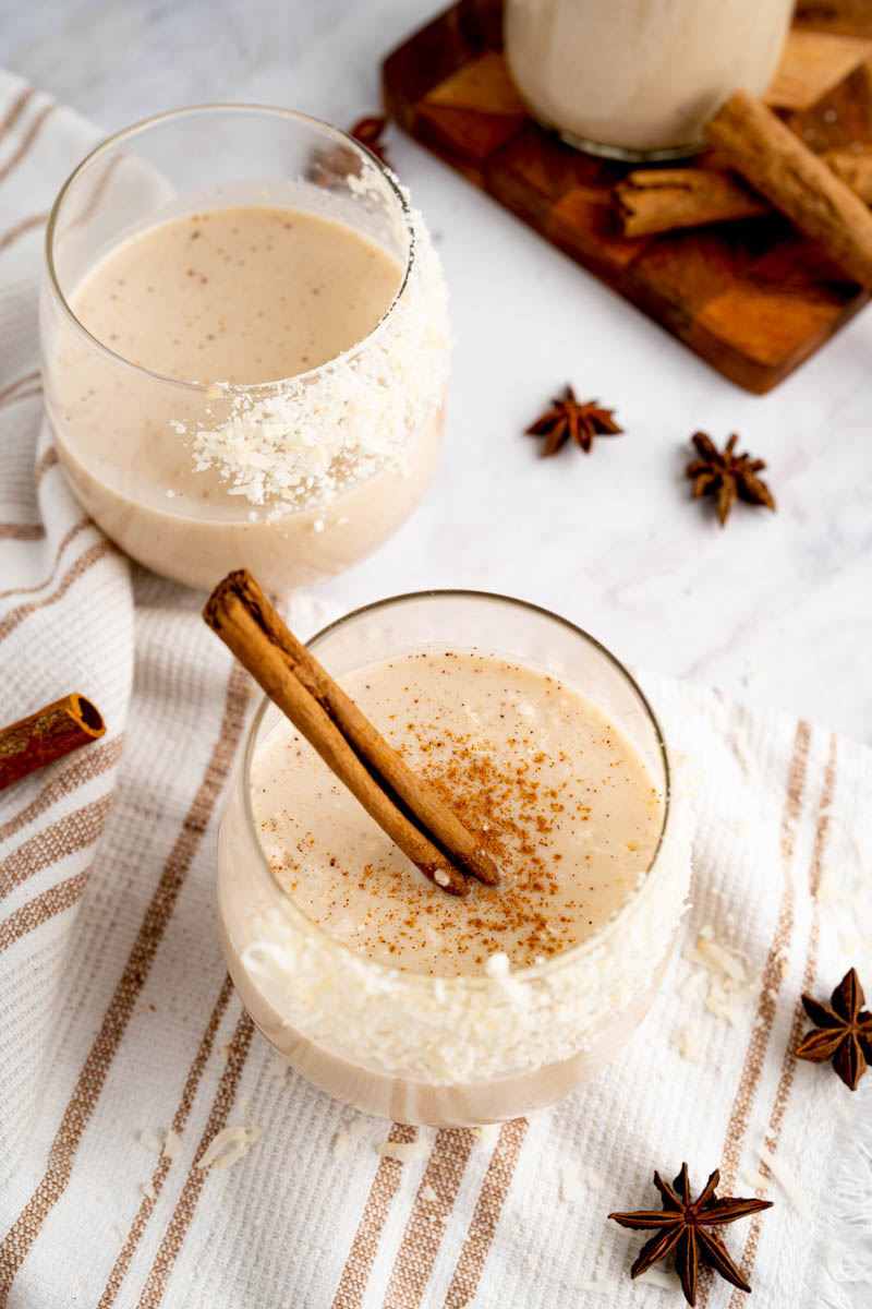 Two glasses of coquito on a white countertop for serving.