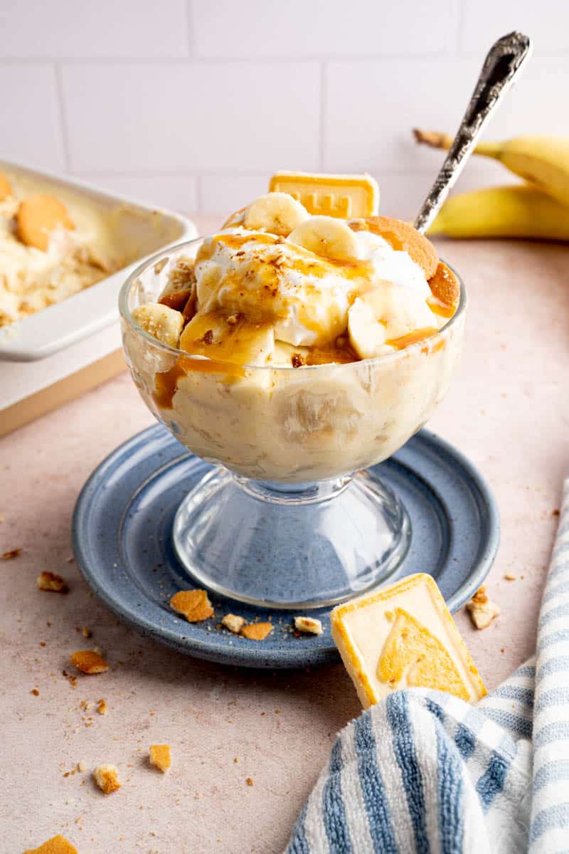 Banana pudding served in a glass serving dish with caramel sauce drizzled on top and a spoon in the dish for eating. 