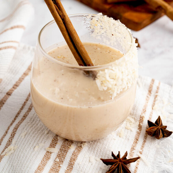 A glass filled with authentic coquito and a cinnamon stick for garnish.
