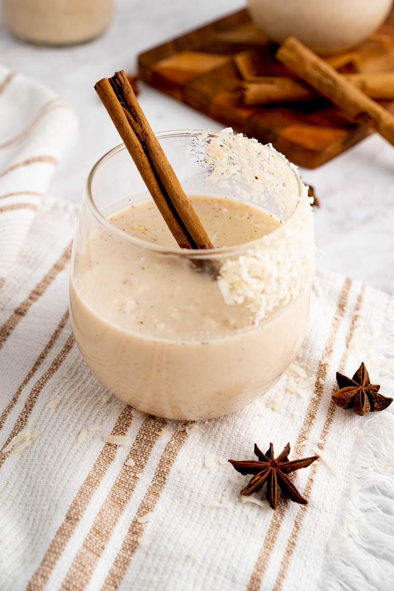 A glass filled with authentic coquito and a cinnamon stick for garnish.