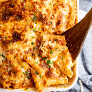 a wooden spoon scoops baked ziti out of a white casserole dish