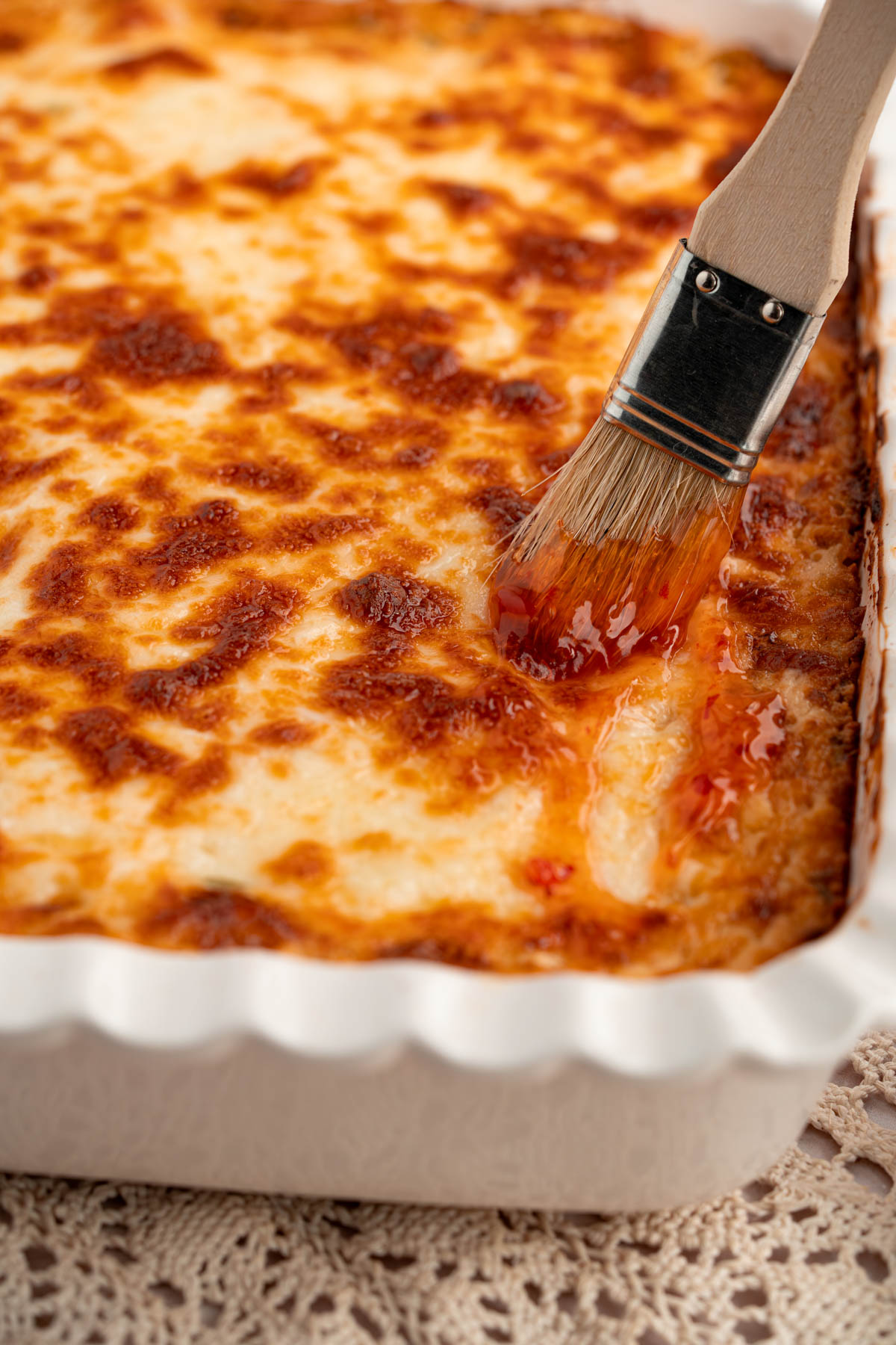 A pastry brush is brushing the baked crab rangoon dip with sweet chili sauce before serving.