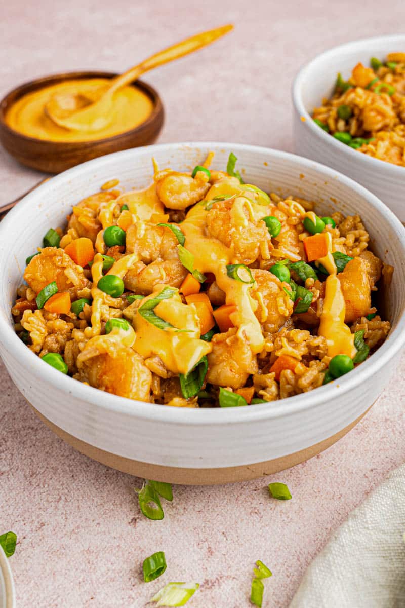 Shrimp fried rice in a bowl with yum yum sauce drizzles on top.
