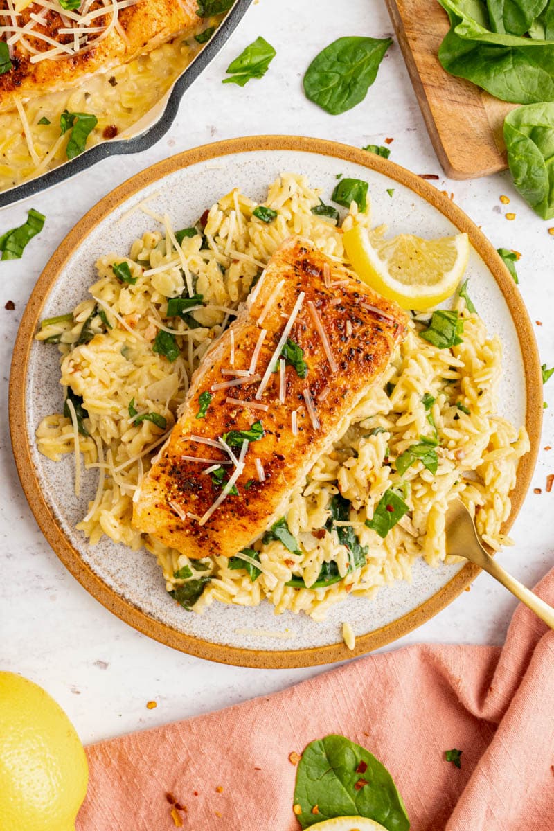 A piece of salmon sits on lemon orzo pasta on a white plate for serving.