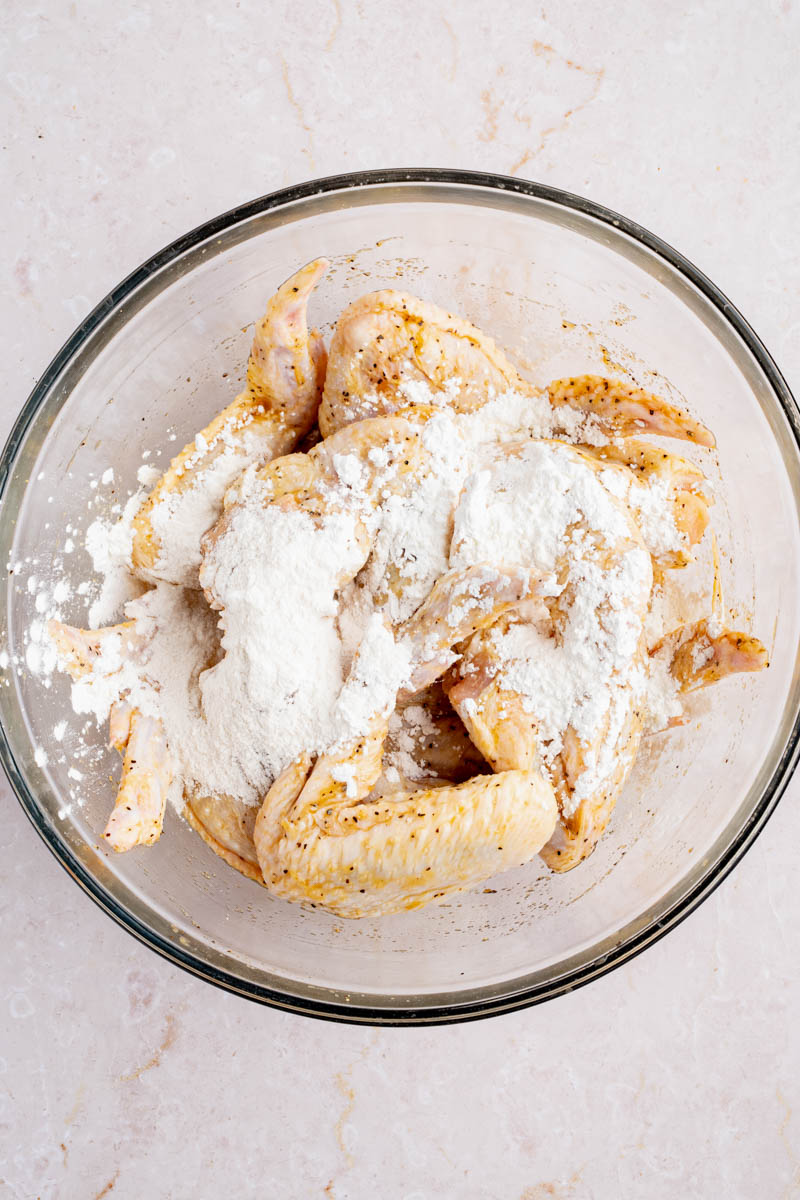 Marinated chicken wings being tossed in cornstarch.