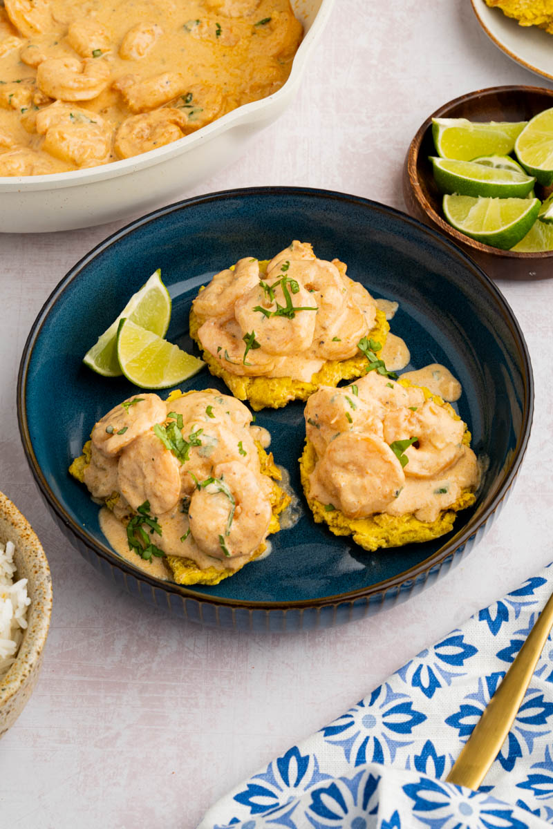 Camarones al ajillo on tostones with a side of lime wedges on a blue plate for serving.