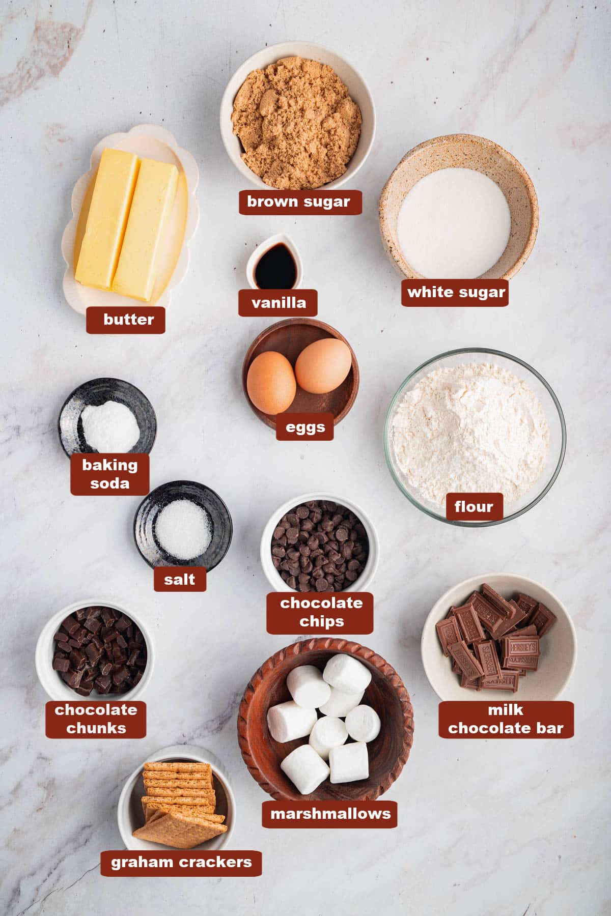 All of the ingredients for S'mores Cookies in bowls on a white countertop.