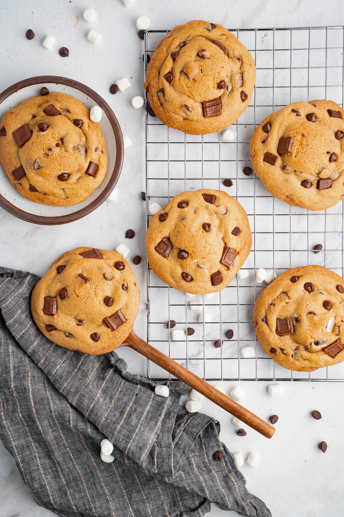 Six baked s’mores cookies sit on a baking rack after coming out of the oven. A spatula is scooping one of the cookies.