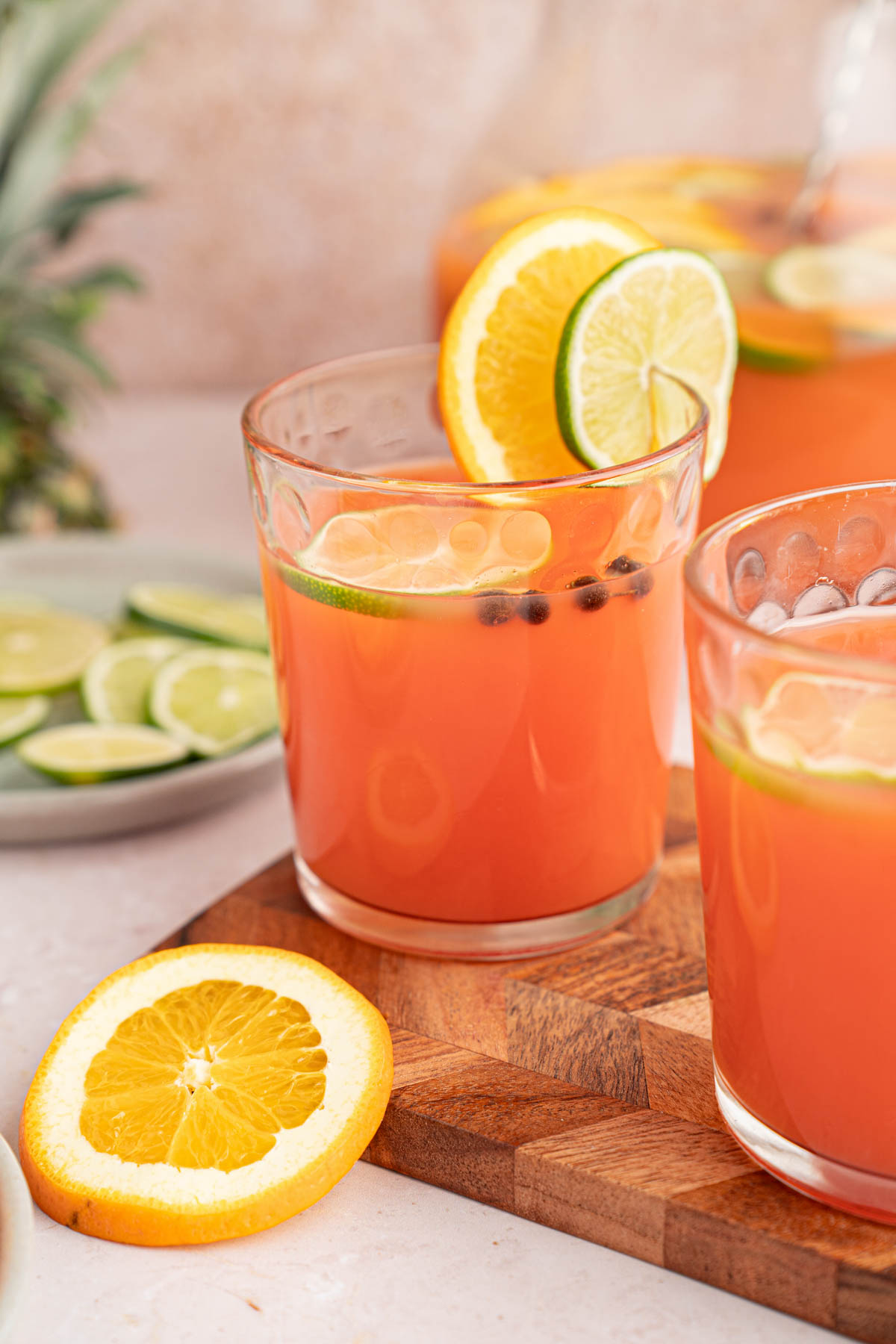 Glass of rum punch with a orange and lime slice garnish sitting on a wooden cutting board.