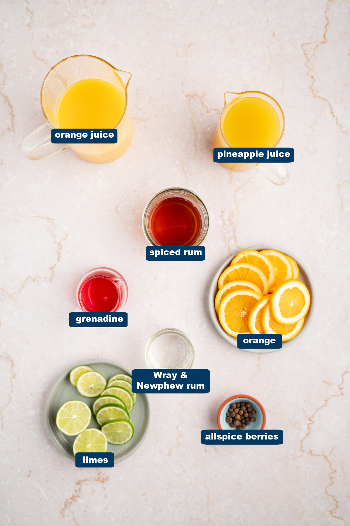 All of the ingredients for rum punch in cups or bowls on a white countertop.