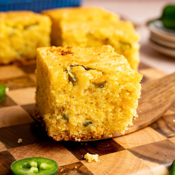 A serving utensil holds a piece of jalapeno cheddar cornbread on top of a wooden cutting board for serving.
