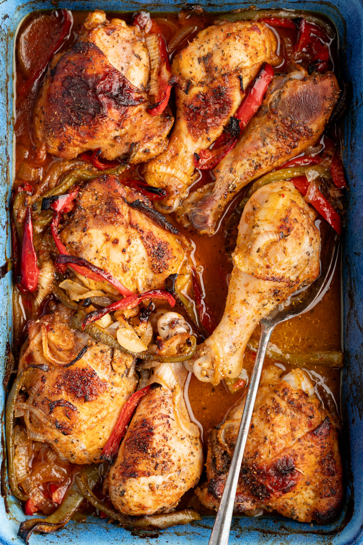 The baked chicken in the pan with the peppers and onions. A serving spoon sits in the pan under the chicken.