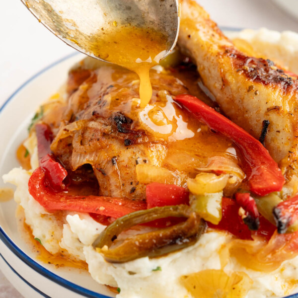 A spoon drizzles some of the sauce over the italian dressing chicken over potatoes.