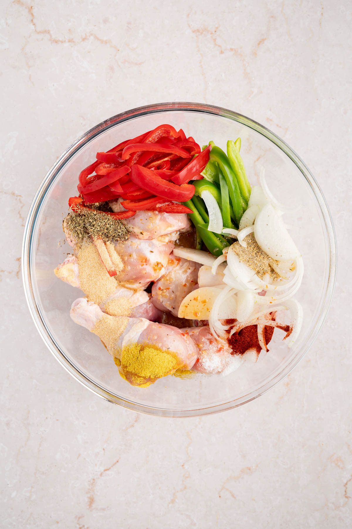 The chicken in a large bowl with the seasonings, peppers and onions before mixing everything together.