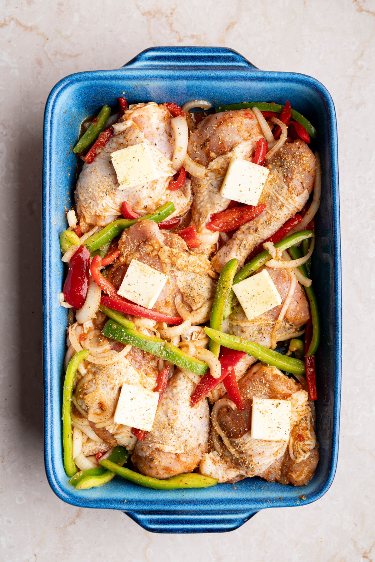 The chicken and italian dressing marinade in a baking dish before going into the oven. Slices of butter are on top of the chicken.