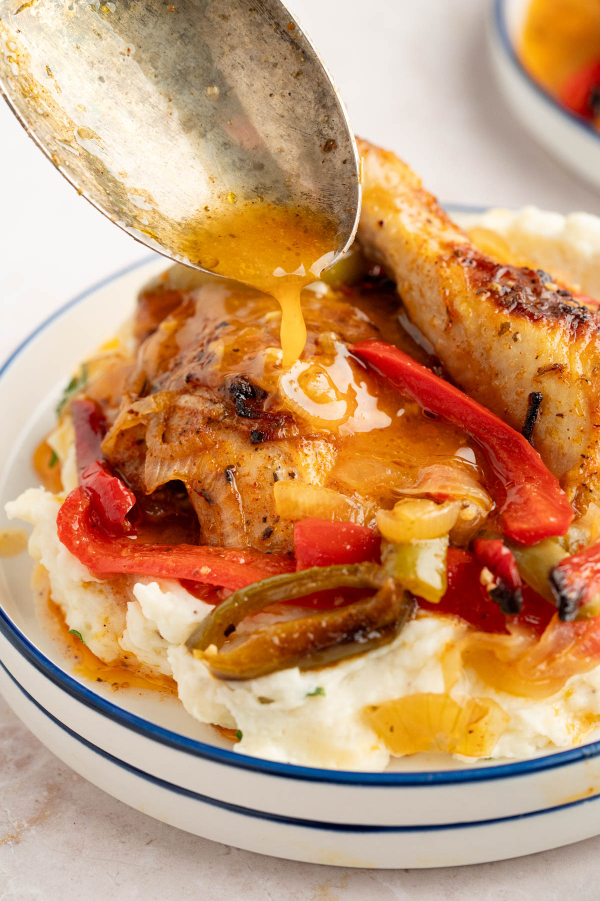 A spoon drizzles some of the sauce over the italian dressing chicken over potatoes.