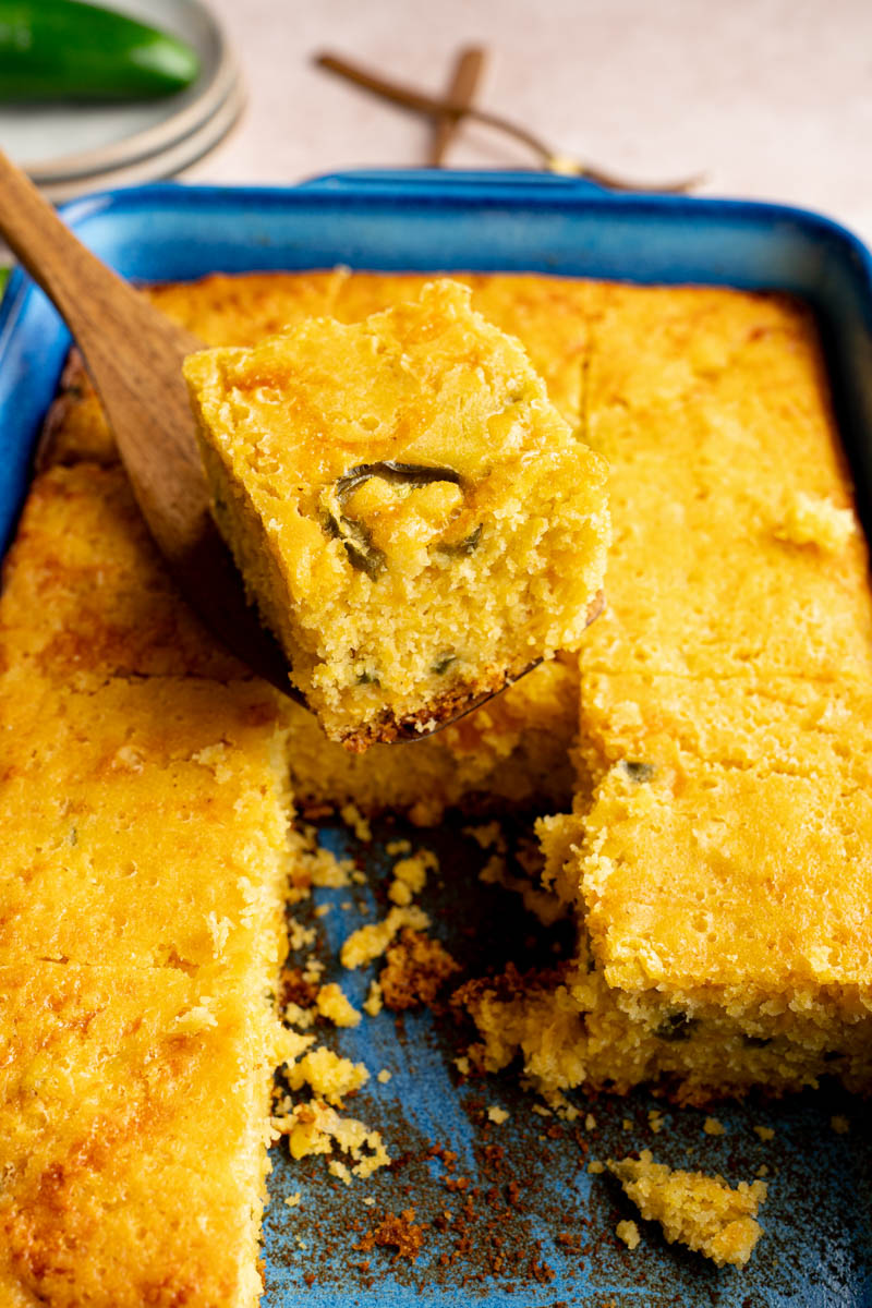 A serving utensil picks up a piece of the jalapeno cheddar cornbread from the baking dish for serving.