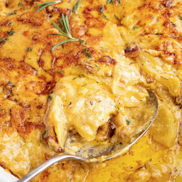 A spoon scoops cheesy au gratin potatoes from a baking dish for serving.