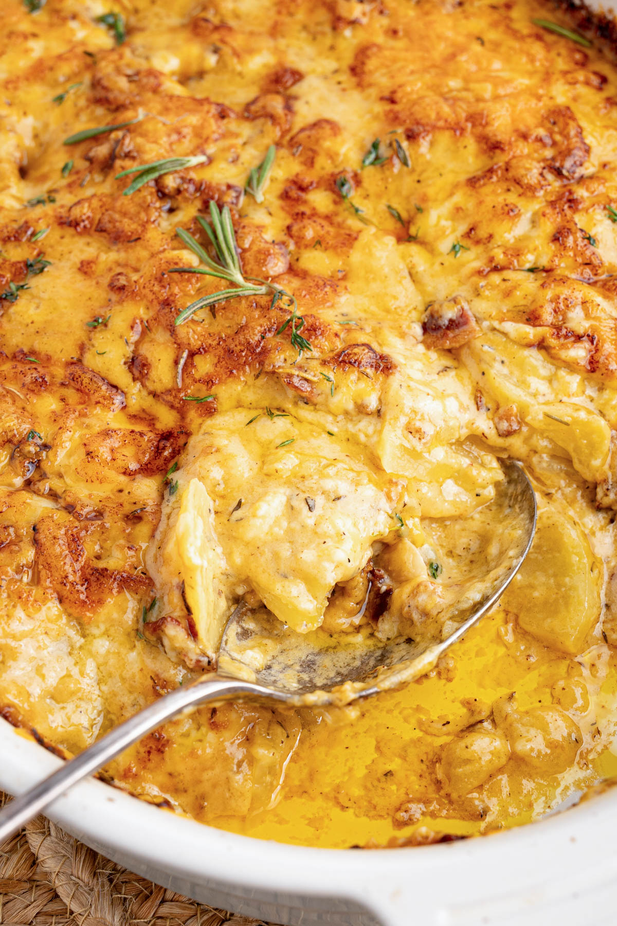 A spoon scoops cheesy au gratin potatoes from a baking dish for serving.