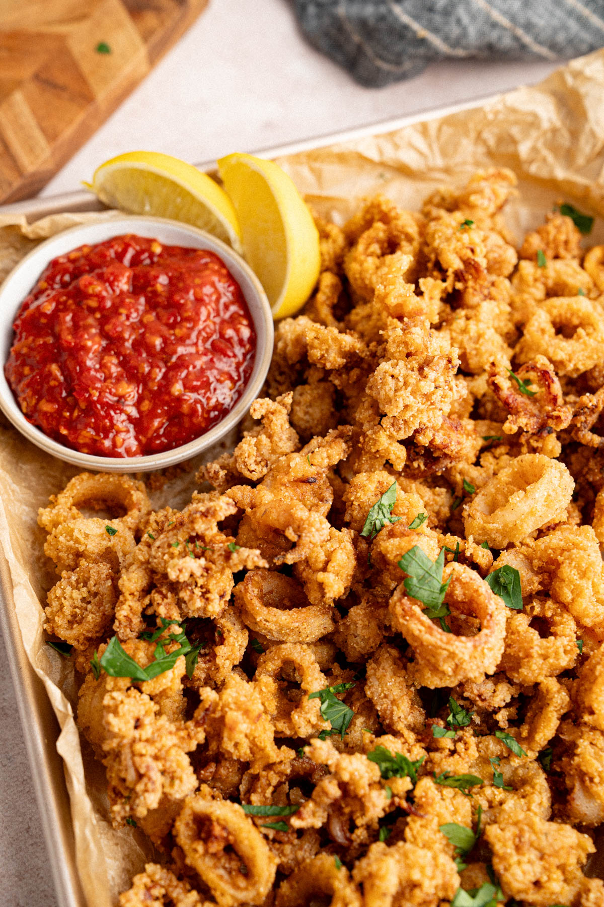 Fried calamari on a pan for serving with a small bowl of marinara sauce and lemon wedges.
