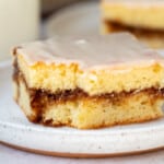 A slice of honey bun cake with a bite taken out of it sitting on a white plate.