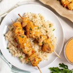 Two bang bang chicken skewers on a plate of white rice for serving.