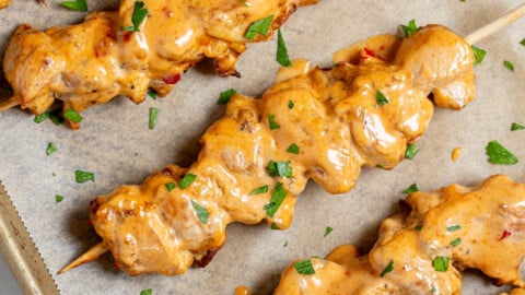 five bang bang chicken skewers on a sheet pan after baking with a small amount of parsley as garnish.