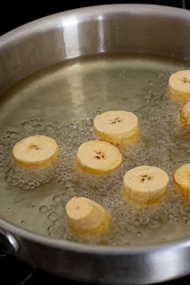 cut green plantains in a skillet for frying