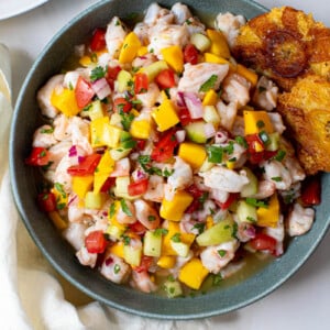 Mango ceviche in a blue bowl with two tostones on the side for serving.