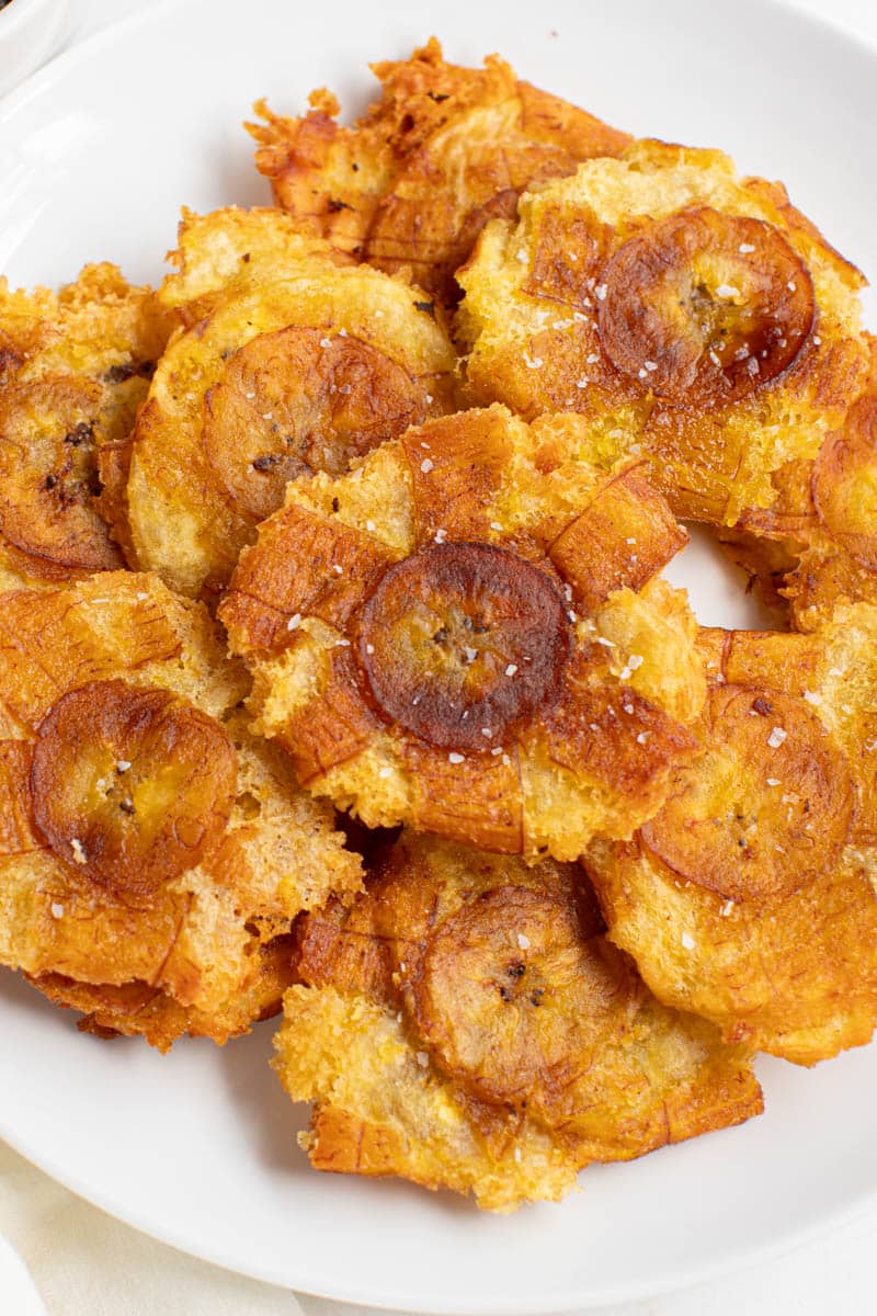Tostones (fried green plantains) piled on a white plate for serving.